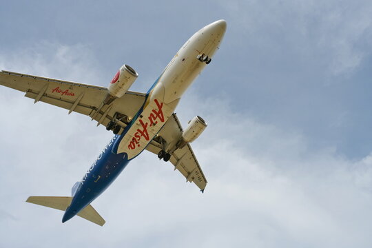 AirAsia planes have white-dark-blue patterns and red letters. Phuket, Thailand, January 25, 2023. Picture of the underbelly of an AirAsia plane while flying in a slightly cloudy sky.
