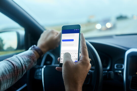 Young man texting on his smartphone while driving his car in the city