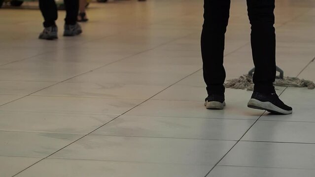 A slow-motion shot of cleaning woman washing the floor in a mall, people walking around. Woman works as a cleaner in a public place.