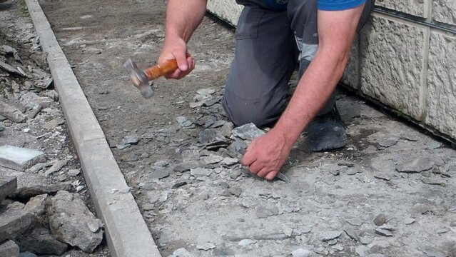 Slow motion video. Worker repairs foundation of building outside on summer day. Hands of bricklayer with hammer and chisel during work.