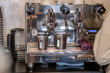 The barista prepares fresh coffee in the coffee machine in the morning in the cafe. There are coffee cups on the table for customers. Coffee machine close-up