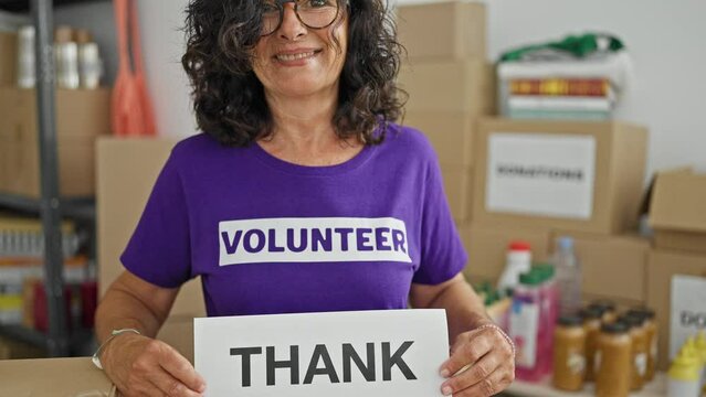 Middle age hispanic woman volunteer smiling confident holding thank you message at charity center - Powered by Adobe