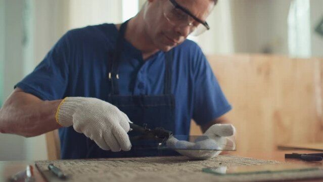 Rack focus of glazier using pliers when working with piece of glass at desk in workshop