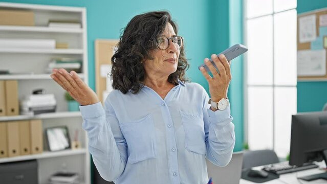 Middle age hispanic woman business worker sending voice message by smartphone working at the office