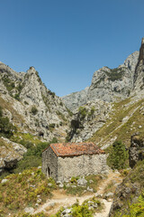 Fototapeta na wymiar A small cobblestone mountain hut with a terracotta roof. The rocky mountains in the background of Spain for a dramatic landscape of Asturias Spain. Magical vertical landscape.