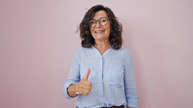 Middle age hispanic woman smiling confident doing ok sign with thumb up over isolated pink background