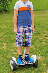 A boy portrait in a T-shirt and sneakers, stands on a hoverboard in a park on the street