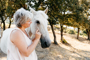 Middle aged woman peting a white horse in countryside