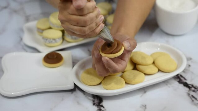 pastry chef's hands filling, decorating and making cornstarch alfajores with dulce de leche and coconut