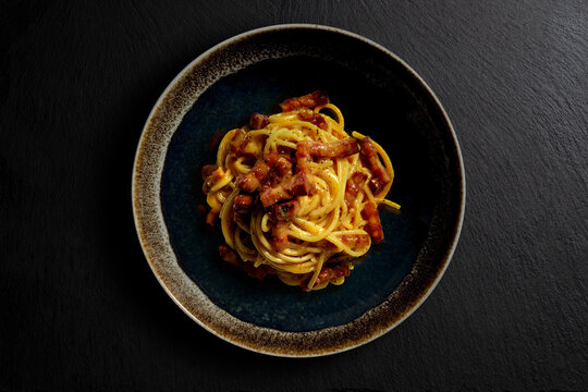 Dark bowl with spaghetti carbonara on black stone