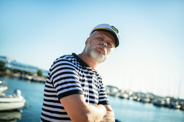 Fototapeta premium Mature man standing near the sea dressed in a sailor's shirt and hat.