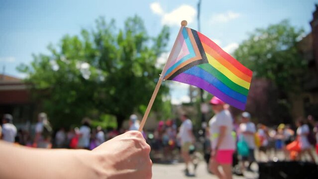 Hand hold Pride Flag and people at pride parade. Close up footage
