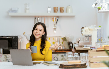 Obraz na płótnie Canvas Beautiful Asian woman smiling happily relaxing using laptop technology Take notes Drink a relaxing hot drink while sitting on the table in your room at home.