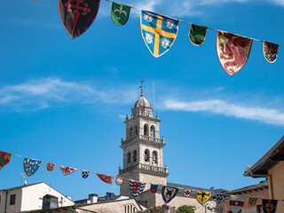 Medieval flags and pennants decorate the streets of Ponferrada during the Encina festivities in Ponferrada on a sunny day and the tower of the Basilica of Nuestra Señora de la Encina in the background
