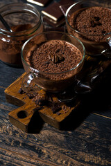 sweet chocolate mousse in glass cups on wooden background, vertical