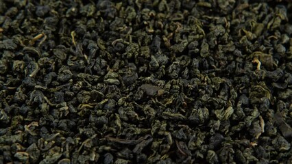 Black Dry Tea Wallpaper. Wooden spoon picks up Mix Black and Green Tea Leaves. Close Up, Macro. Top View. Texture. Copy Space. Dried Tea is Spinning, Rotating on Turntable. Food and Drink Background	
