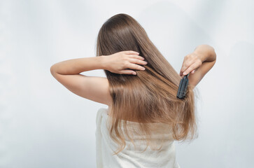 Back view of beautiful woman combing her hair with brush on white background