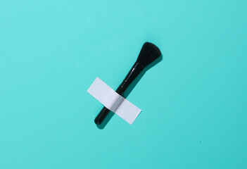 Makeup brush is taped to a blue wall. Conceptual beauty photo, minimalism.