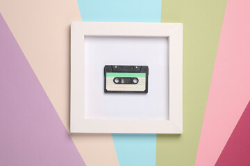 Retro 80s audio cassette in white square frame on colored background. Aesthetic minimal still life. Conceptual photo. Modern art. Top view