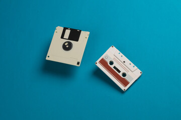 White floppy disk and audio cassette on a blue background. Retro technology. Top view