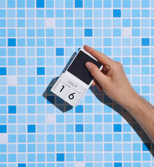 Man's hand holding wooden block calendar with date July 16 on tile background