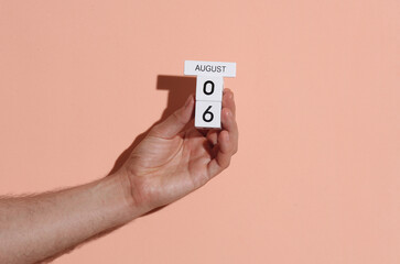 Man's hand holding wooden block calendar with date august 6 on pink bright background