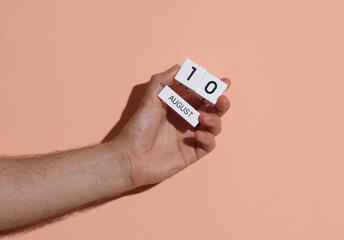 Man's hand holding wooden block calendar with date august 10 on pink bright background