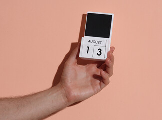 Man's hand holding wooden block calendar with date august 13 on pink bright background