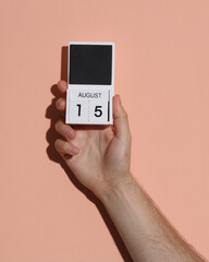 Man's hand holding wooden block calendar with date august 15 on pink bright background