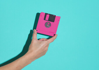 Hand holding pink retro 80s floppy disk on a blue background