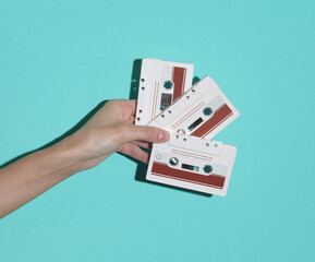 Female hand holding retro 80s audio cassettes on blue background with shadow