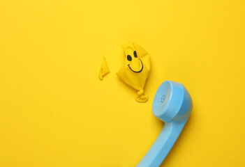 Retro telephone receiver and yellow Burst balloon with smiling face on yellow background. - obrazy, fototapety, plakaty