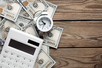 Many dollar bills with alarm clock and calculator on a wooden table. Business concept. Time is money