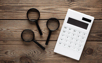 Calculator with magnifiers on wooden background. Top view