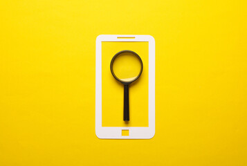 Paper-cut smartphone icon with magnifying glass on a yellow background. Searching for information on the Internet