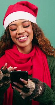 Beautiful young woman in Santa hat texts and uses phone laughing, Xmas studio