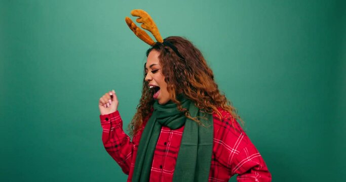 Happy young woman dancing in studio, Christmas reindeer ears dress up