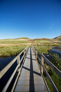 Wooden boardwalk with railing over a river with a blue sky; Cheviot hills northumberland england