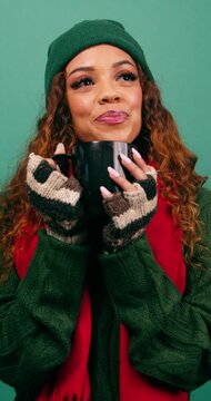 Beautiful young woman sips warm drink in winter, Christmas colours studio
