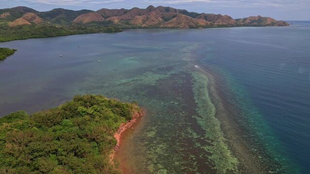Drone footage of Coastline and recife in  in Coron in Philippines. We do a simple dolly movement to catch the beautifulness of the recife and beach nearby. There is mountains in the landscape behind