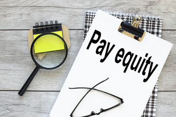 Pay Equity. text on white a4 paper. magnifier and sticker beautiful notepad
