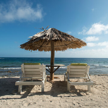 Two Chairs Under An Umbrella On The Beach; Utopia Village, Utila, Bay Islands, Honduras