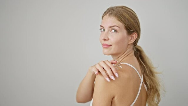 Young blonde woman smiling confident applying lotion on skin over isolated white background