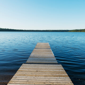 Fototapeta A Wooden Dock Leading Out To A Lake And Blue Sky In Riding Mountain National Park  Wasagaming, Manitoba, Canada