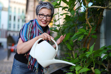 A mature and happy woman, an avid gardener, enjoying her summer hobby of watering plants outdoors.