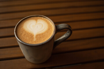 A cappuccino cup on a wooden table. Coffee in a clay mug. A heart on a cappuccino foam. Place to copy