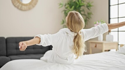 Young blonde woman waking up stretching arms at bedroom
