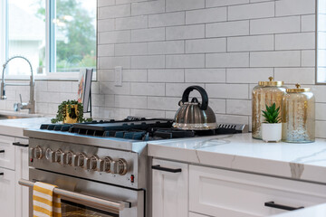 Modern kitchen details of large gas range with teapot and yellow and white towel near marble...