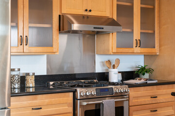 Modern kitchen details of honey wood cabinets with gas range and black counters.