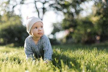 A beautiful baby sits on the green grass outside. High quality photo